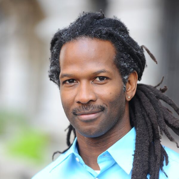 A photo of Carl Hart wearing a blue button down shirt with a blurred background, smiling slightly.
