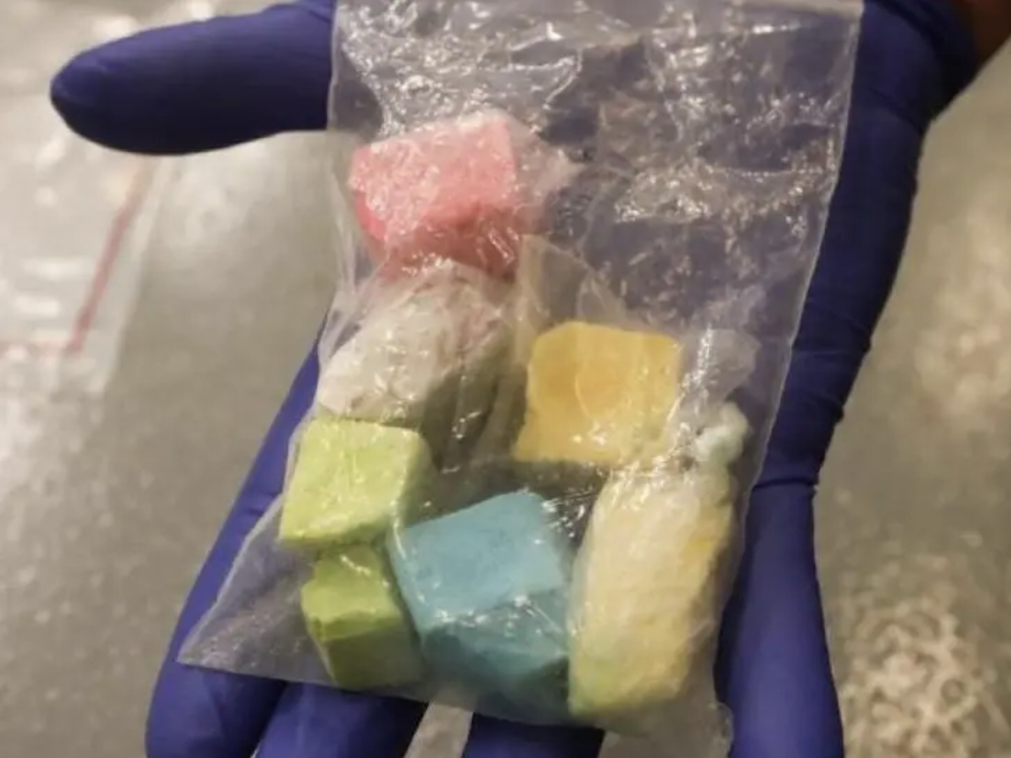 A photo of chunks of rainbow fentanyl in a plastic baggie on a gloved hand.